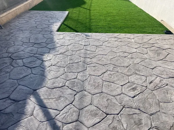 Patio con hormigón impreso de piedra irregular gris junto a césped